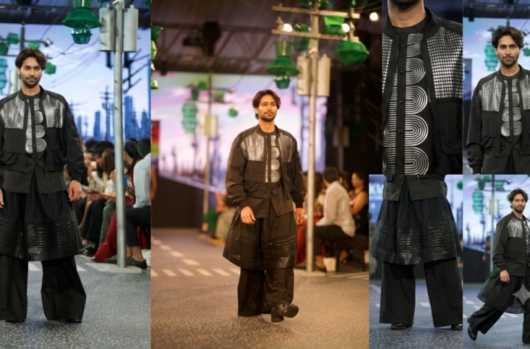 Male model on a runway wearing a black outfit with silver geometric panels and a wide, layered skirt-like coat.